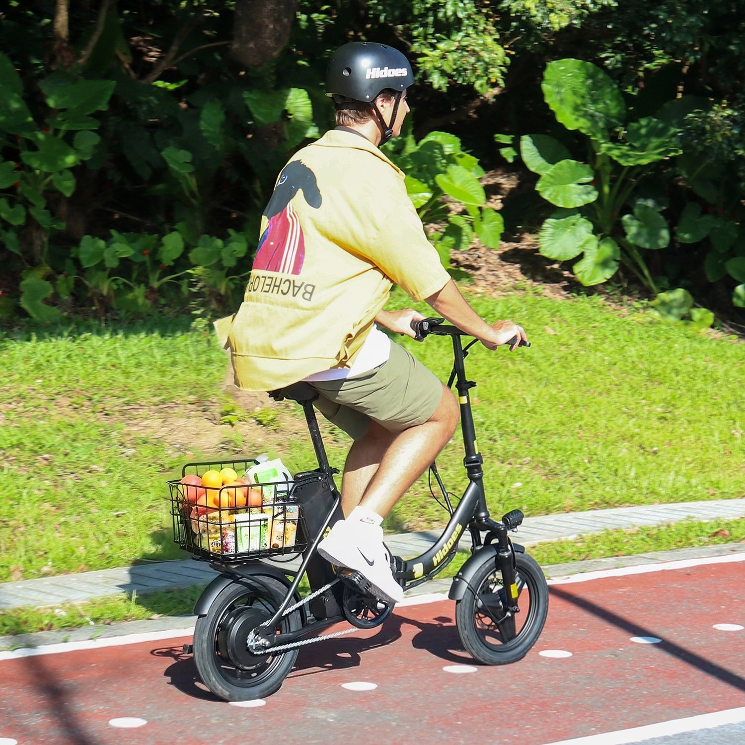 Person riding a Hidoes C5 small electric bike with a basket on a path surrounded by greenery